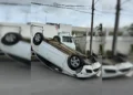 Carro de passeio de cor prata capotado com as quatro rodas para cima no meio de uma rua residencial asfáltica em Santo Antônio de Jesus