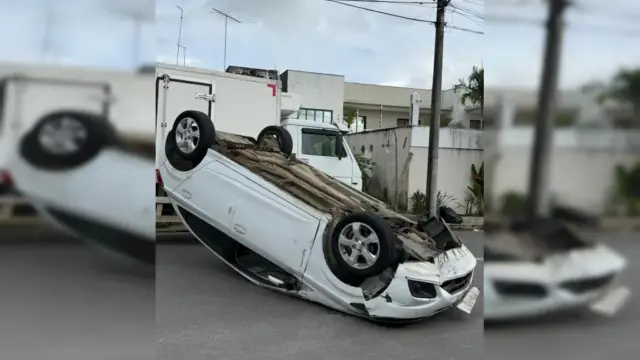 Carro de passeio de cor prata capotado com as quatro rodas para cima no meio de uma rua residencial asfáltica em Santo Antônio de Jesus