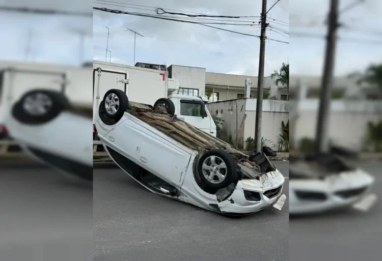 Carro de passeio de cor prata capotado com as quatro rodas para cima no meio de uma rua residencial asfáltica em Santo Antônio de Jesus