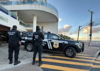 Carro da Polícia Civil com dois policiais parados em frente a uma residência