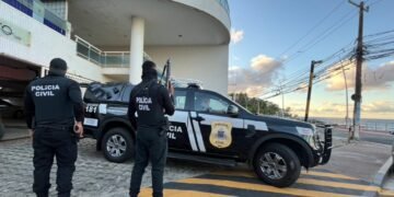 Carro da Polícia Civil com dois policiais parados em frente a uma residência