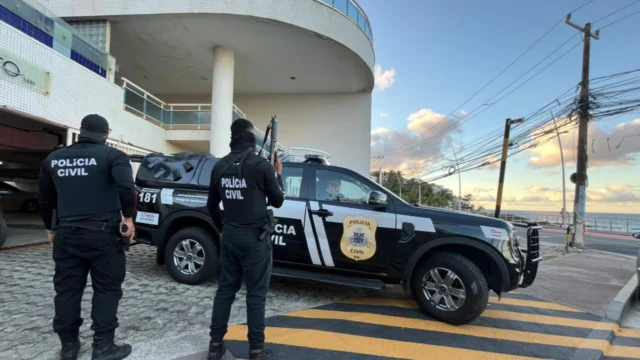 Carro da Polícia Civil com dois policiais parados em frente a uma residência