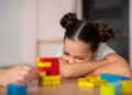 criança debruçada sobre os braços observando brinquedos educativos sobre a mesa