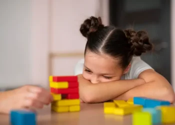 criança debruçada sobre os braços observando brinquedos educativos sobre a mesa